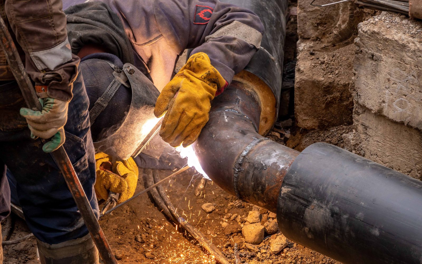 Handwerker beim Verschweißen einer Heizungsrohrleitung, Funkenflug im Werkstattlicht