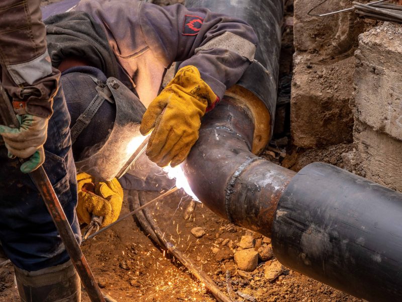 Handwerker beim Verschweißen einer Heizungsrohrleitung, Funkenflug im Werkstattlicht